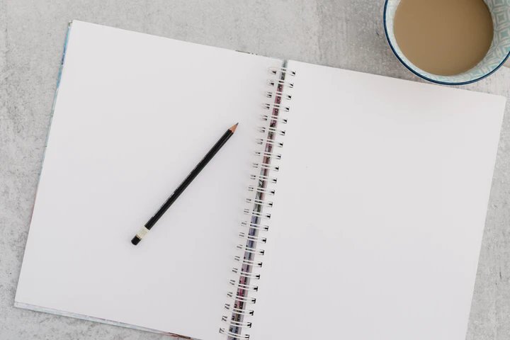 Pencil on notepad with ring binder and a cup of tea beside it.